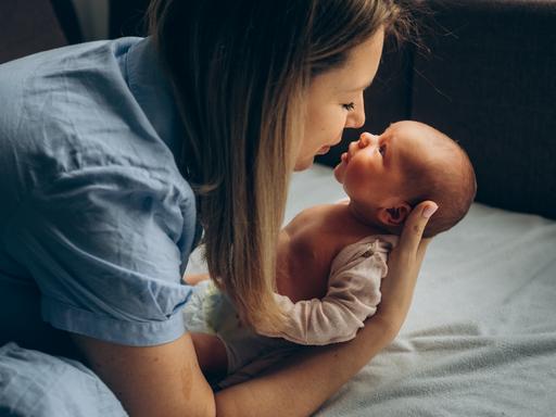 Ein neugeborenes Baby wird von seiner Mutter im Arm gehalten, die beiden schauen sich in die Augen.