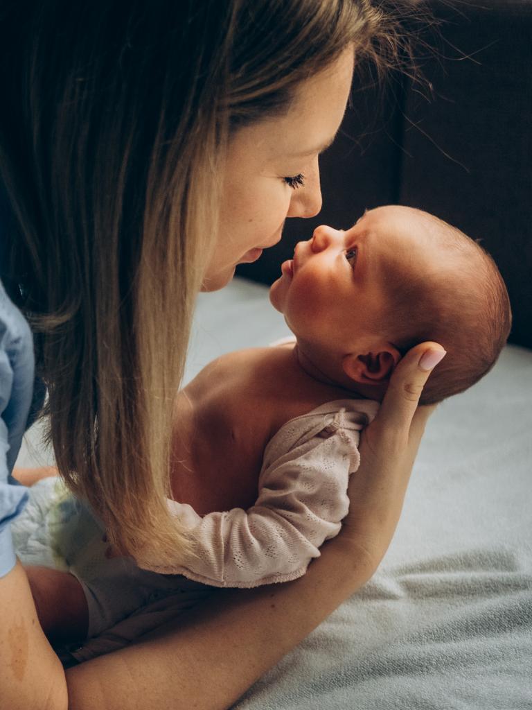 Ein neugeborenes Baby wird von seiner Mutter im Arm gehalten, die beiden schauen sich in die Augen.