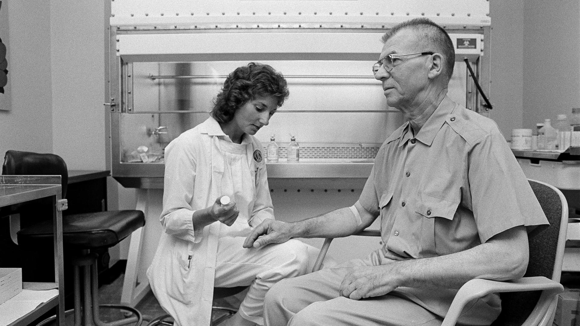 Ein Schwarz-Weiß Foto zeigt eine Onkologiekrankenschwester, die einen männlichen Patienten auf eine Chemotherapie vorbereitet. 