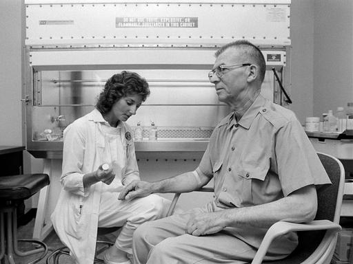 Ein Schwarz-Weiß Foto zeigt eine Onkologiekrankenschwester, die einen männlichen Patienten auf eine Chemotherapie vorbereitet. 