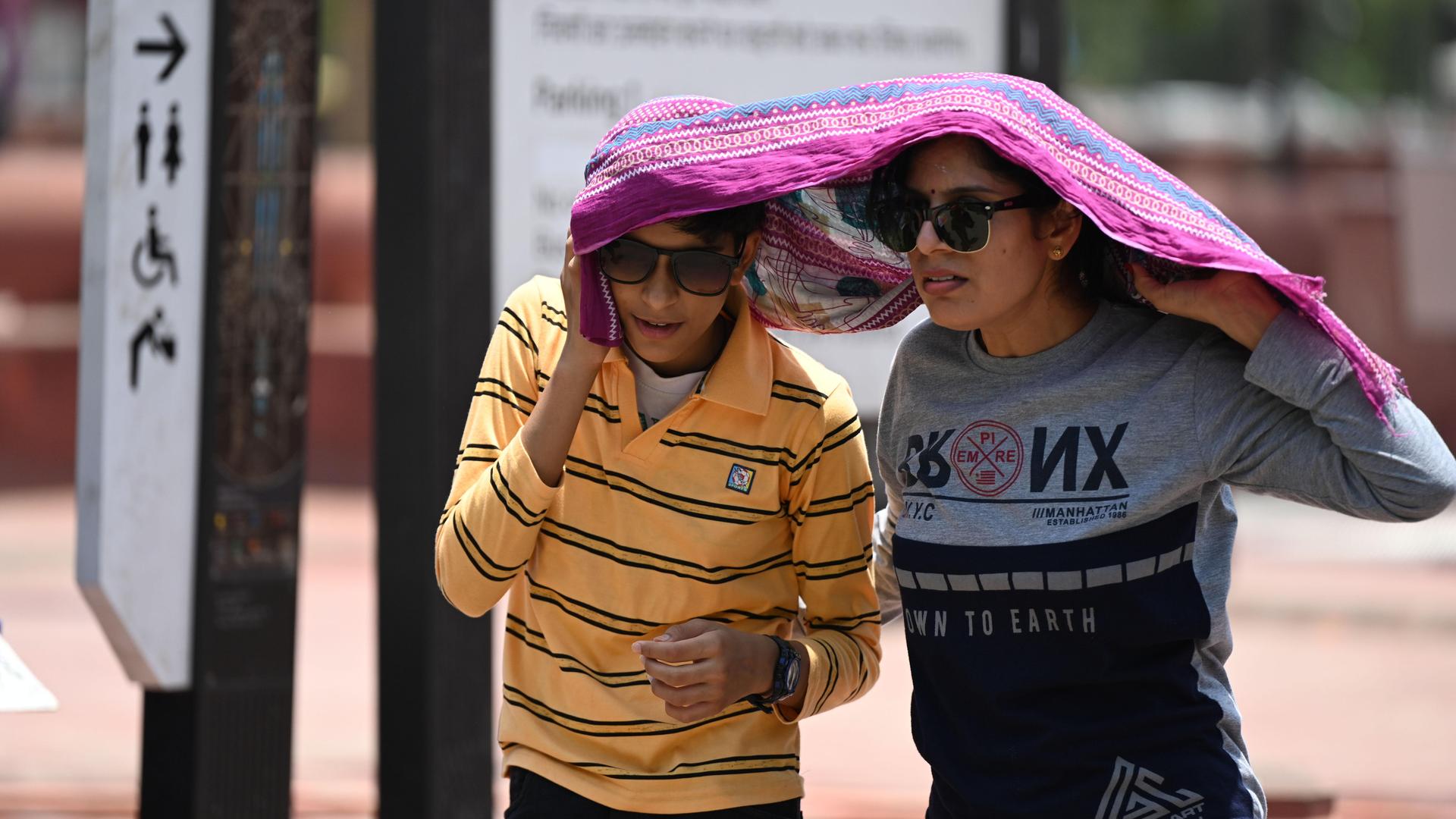 Ein Mann und eine Frau in Deu-Delhi haben sich zum Schutz vor der Sonne ein Tuch über den Kopf gezogen.
