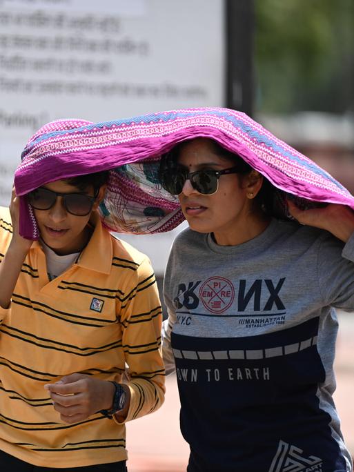 Ein Mann und eine Frau in Deu-Delhi haben sich zum Schutz vor der Sonne ein Tuch über den Kopf gezogen.