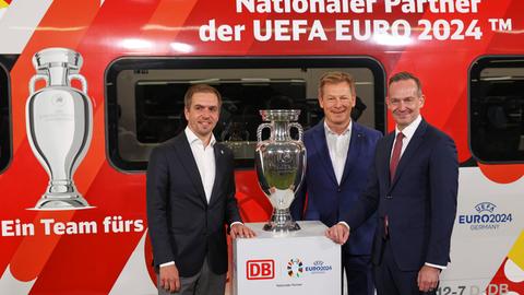 EM-Botschafter Philipp Lahm, DB-Chef Richard Lutz und Volker Wissing, Bundesverkehrsminister, stehen bei der Bekanntgabe der Partnerschaft zwischen Deutscher Bahn und der UEFA zur Europameisterschaft 2024 vor dem EM-Pokal und einem ICE.