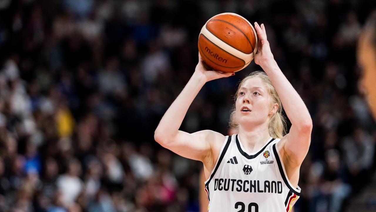 Eine Frau mit roten Haaren und einem weißen Trikot hebt einen Basketball.