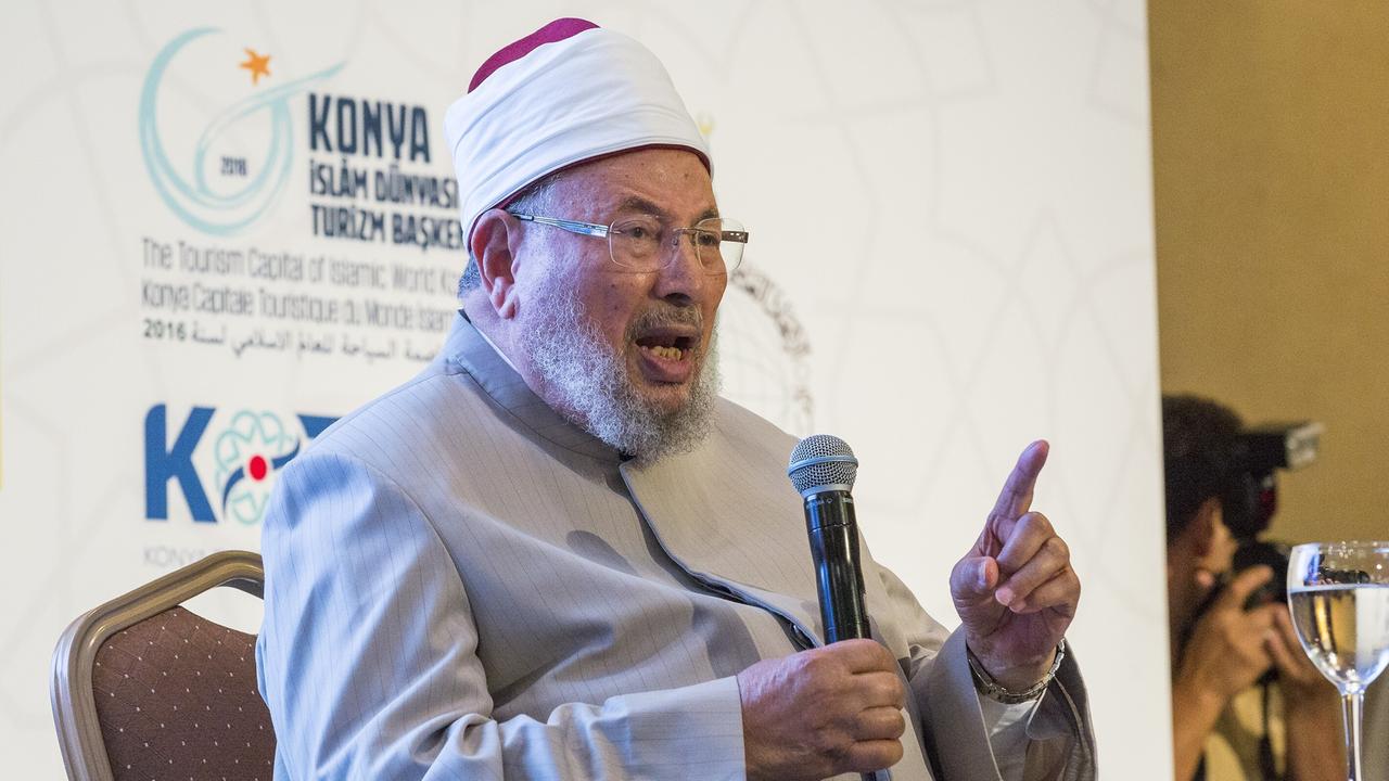 Yusuf al-Qaradawi sitzt auf einer Bühne und hält eine Rede. Aus den Abbildungen an der Wand im Hintergrund ergibt sich, dass es sich um ein Treffen der International Union of Muslim Scholars (IUMS) handelt, im türkischen Konya am 3. August 2016. 