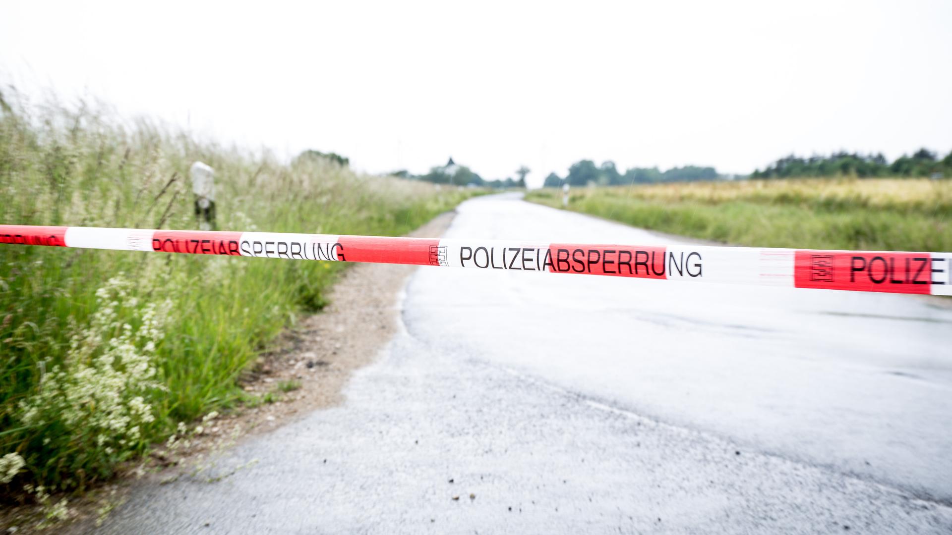 Ein rot-weiß gestreiftes Polizeiband ist quer über eine Landstraße gespannt.