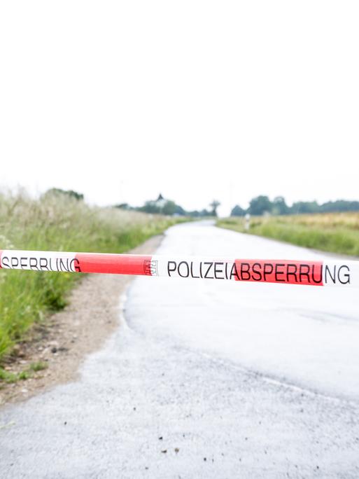 Ein rot-weiß gestreiftes Polizeiband ist quer über eine Landstraße gespannt.