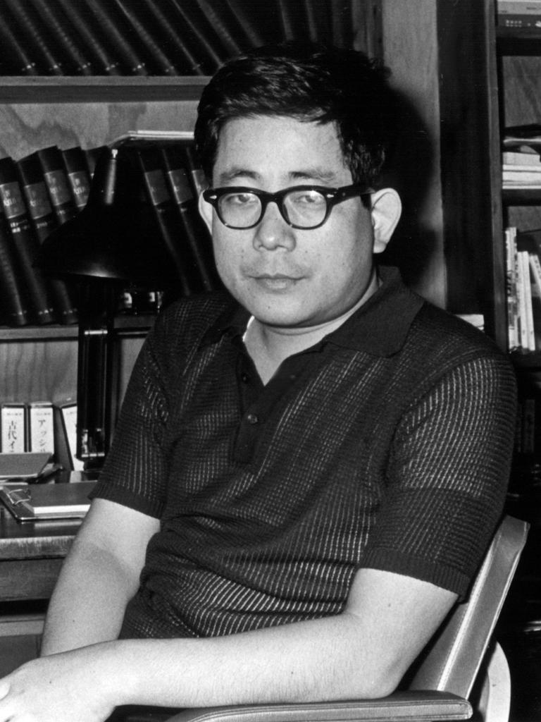 Schwarzweißfoto von Kenzaburo Oe, der als junger Mann an seinem Schreibtisch sitzt. Im Hintergrund ein Bücherregal.