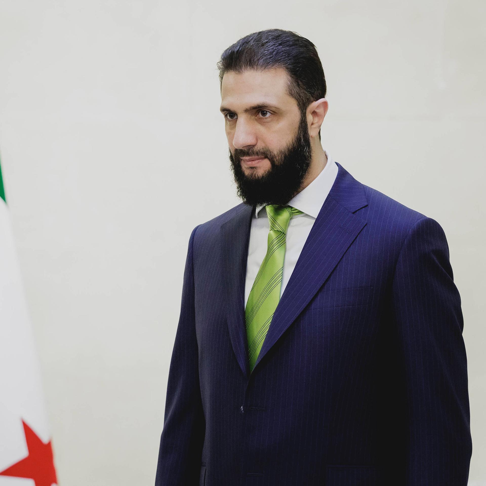 Ahmad Al-Scharaa steht neben der Flagge Syriens