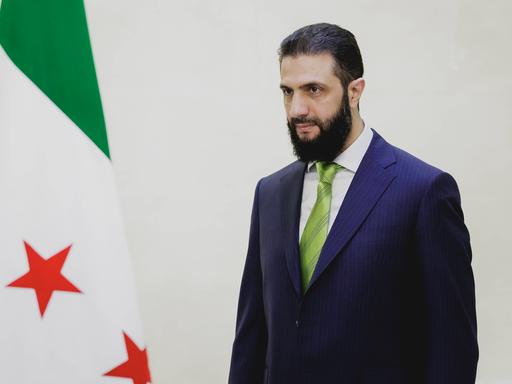 Ahmad Al-Scharaa steht neben der Flagge Syriens