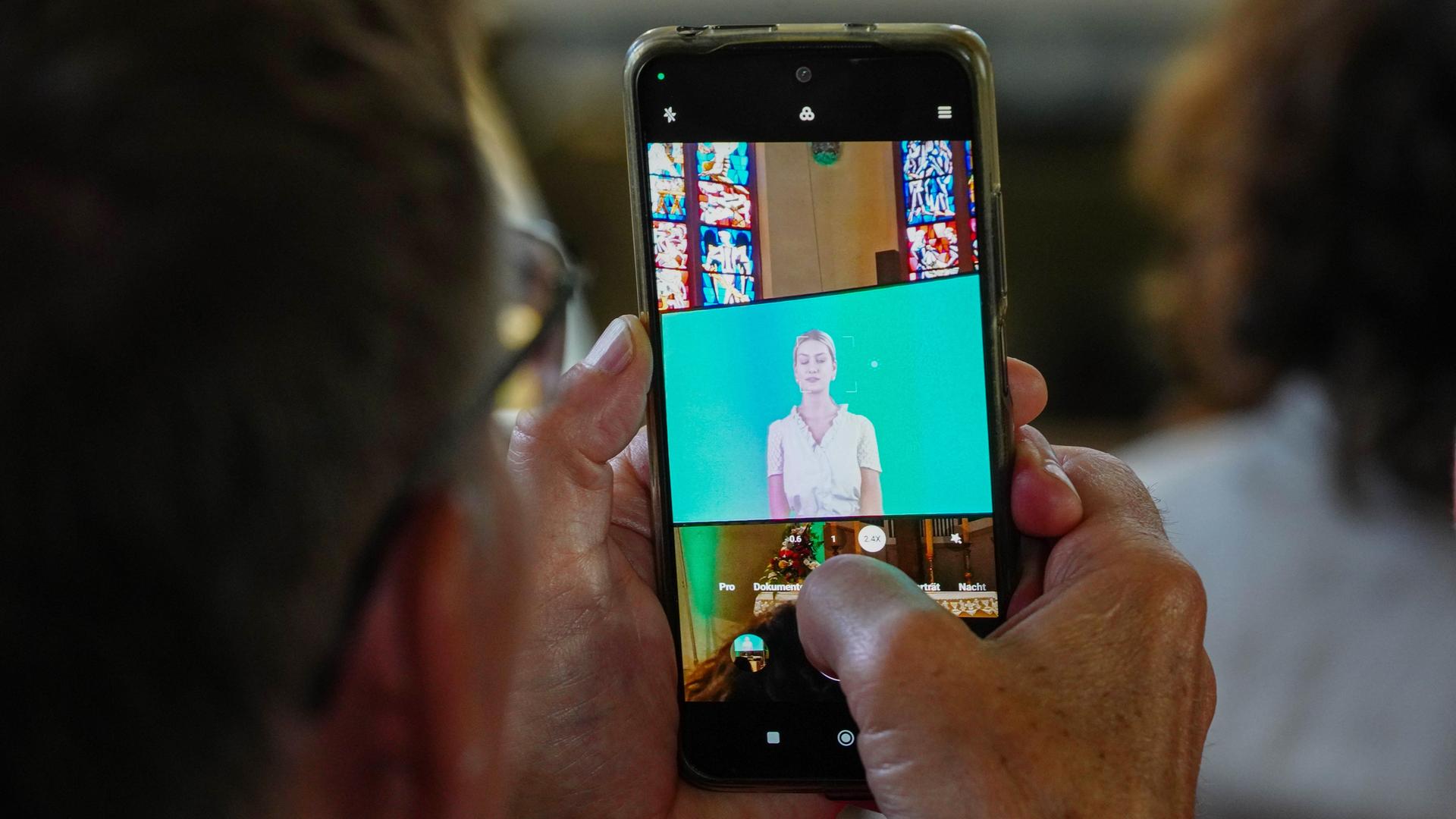 Ein Mann hält ein Smartphone in der Hand, auf dem eine KI-generierte Predigt abgespielt wird.