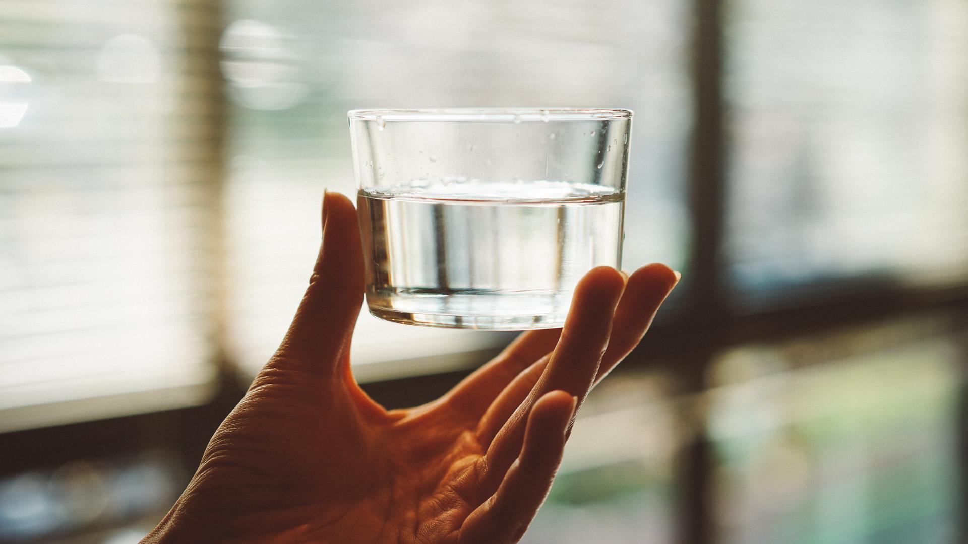 Eine Hand hält ein Wasserglas. Es ist halb voll.