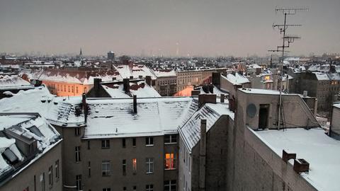 Die Dächer von Berlin im Winter, mit Schnee bedeckt und erleuchteten Fenstern.