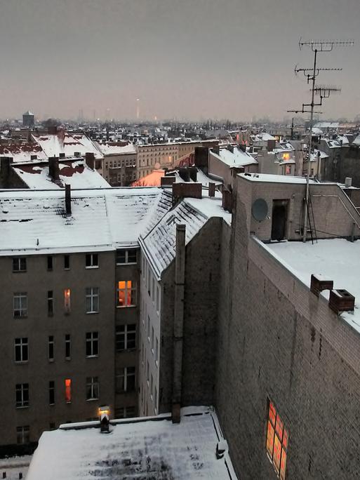 Die Dächer von Berlin im Winter, mit Schnee bedeckt und erleuchteten Fenstern.