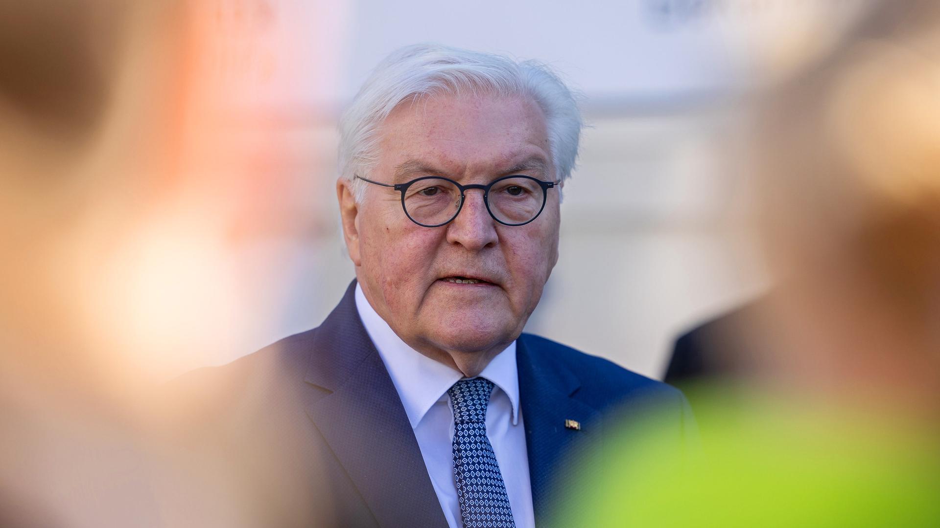 Bundespräsident Frank-Walter Steinmeier in Großaufnahme, rundherum verschwommen mehrere Menschen. 