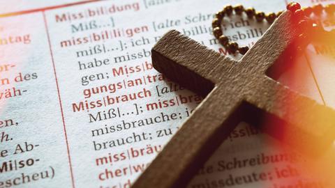 Symbolbild: Ein Kreuz auf einem Wörterbuch mit dem Wort Missbrauch.
