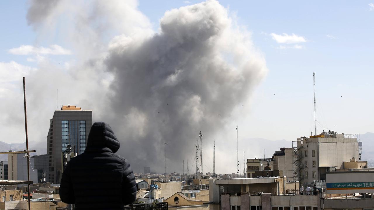 Angriff auf Teheran: Ein Mann schaut von einem Häuserdach über die Dächer der iranischen Hauptstadt. Im Hintergrund steigt nach einem Luftschlag Rauch auf. 