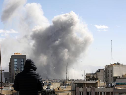 Angriff auf Teheran: Ein Mann schaut von einem Häuserdach über die Dächer der iranischen Hauptstadt. Im Hintergrund steigt nach einem Luftschlag Rauch auf. Angriff auf Teheran: Ein Mann schaut von einem Häuserdach über die Dächer der iranischen Hauptstadt. Im Hintergrund steigt nach einem Luftschlag Rauch auf.