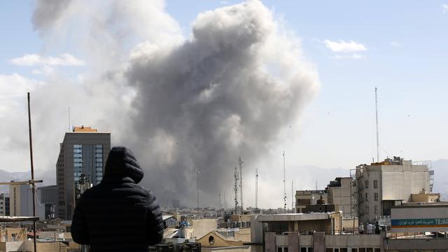 Angriff auf Teheran: Ein Mann schaut von einem Häuserdach über die Dächer der iranischen Hauptstadt. Im Hintergrund steigt nach einem Luftschlag Rauch auf. 