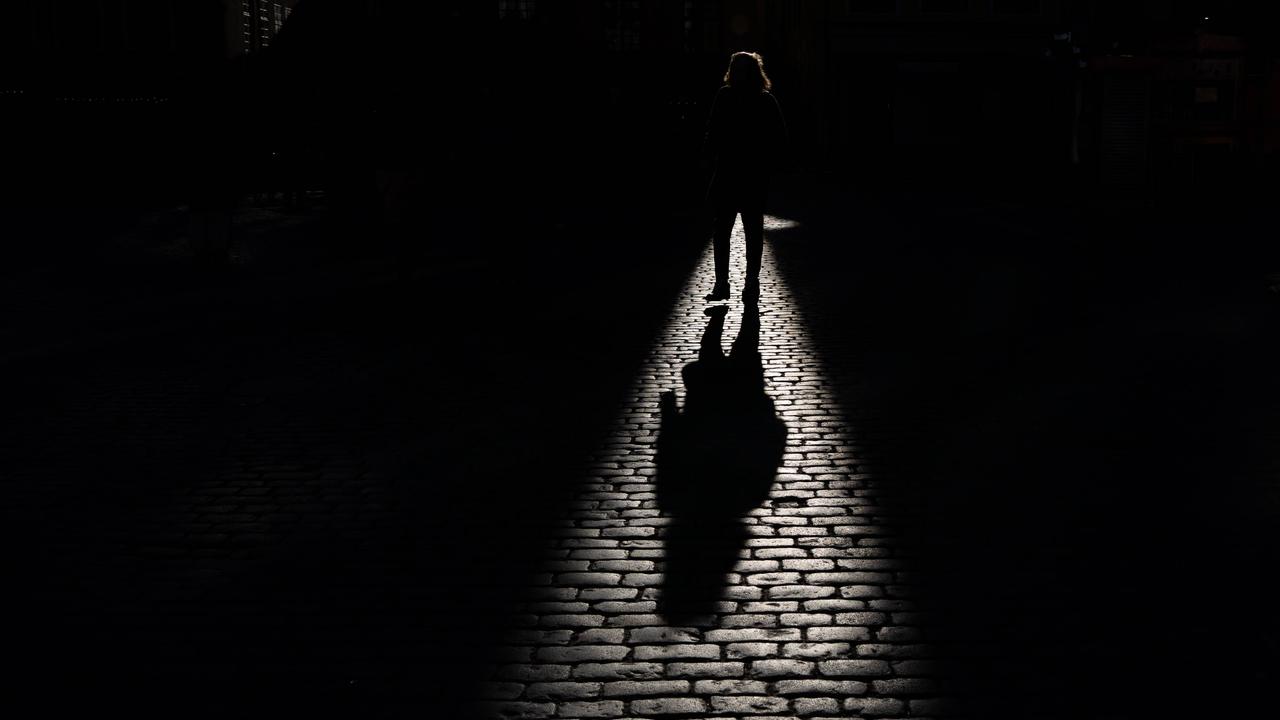 Schatten einer gehenden Person, der auf ein Kopfsteinpflaster fällt. Die Person selbst ist überwiegend im dunklen Bereich und ist nicht genauer zu erkennen. 