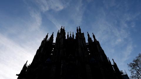 Der Kölner Dom ragt dunkel in einen blauen Himmel hinein.