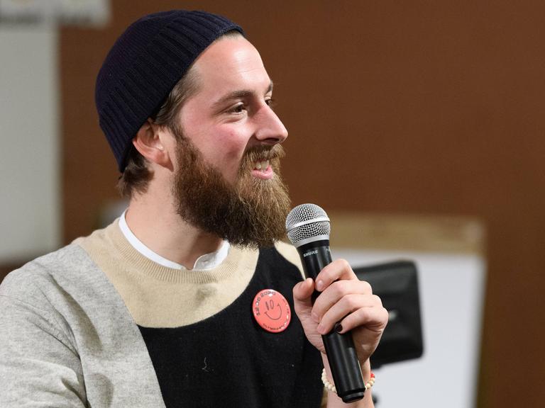 Philip Siefer spricht auf einem Podium bei einer Veranstaltung in Berlin in ein Mikrofon.