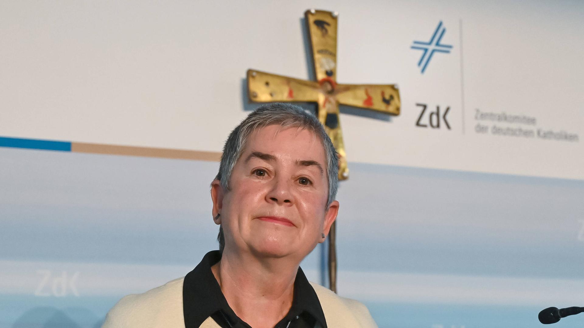 Eine ältere Frau steht vor einem an der Wand hängenden christlichen Kreuz. Eine ältere Frau steht vor einem an der Wand hängenden christlichen Kreuz.