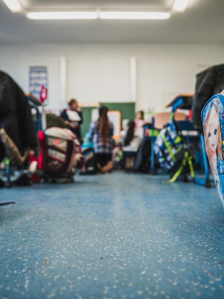 Blick in einen Klassenraum, wo an den Schultischen Schultaschen stehen und Schüler sitzen und stehen.