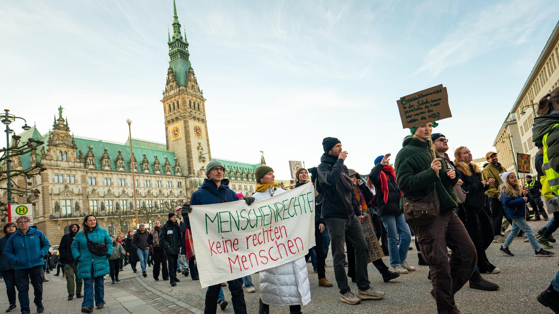 Demonstranten ziehen mit Plakaten unter anderem mit der Aufschrift "Menschenrechte - keine rechten Menschen" vor dem Hamburger Rathaus entlang.