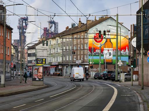 Ein Straße, durchzogen von Straßenbahnschinen. Häuser und im Hintergrund Schornsteine und Industriegebäude