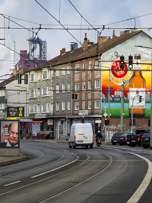 Ein Straße, durchzogen von Straßenbahnschinen. Häuser und im Hintergrund Schornsteine und Industriegebäude