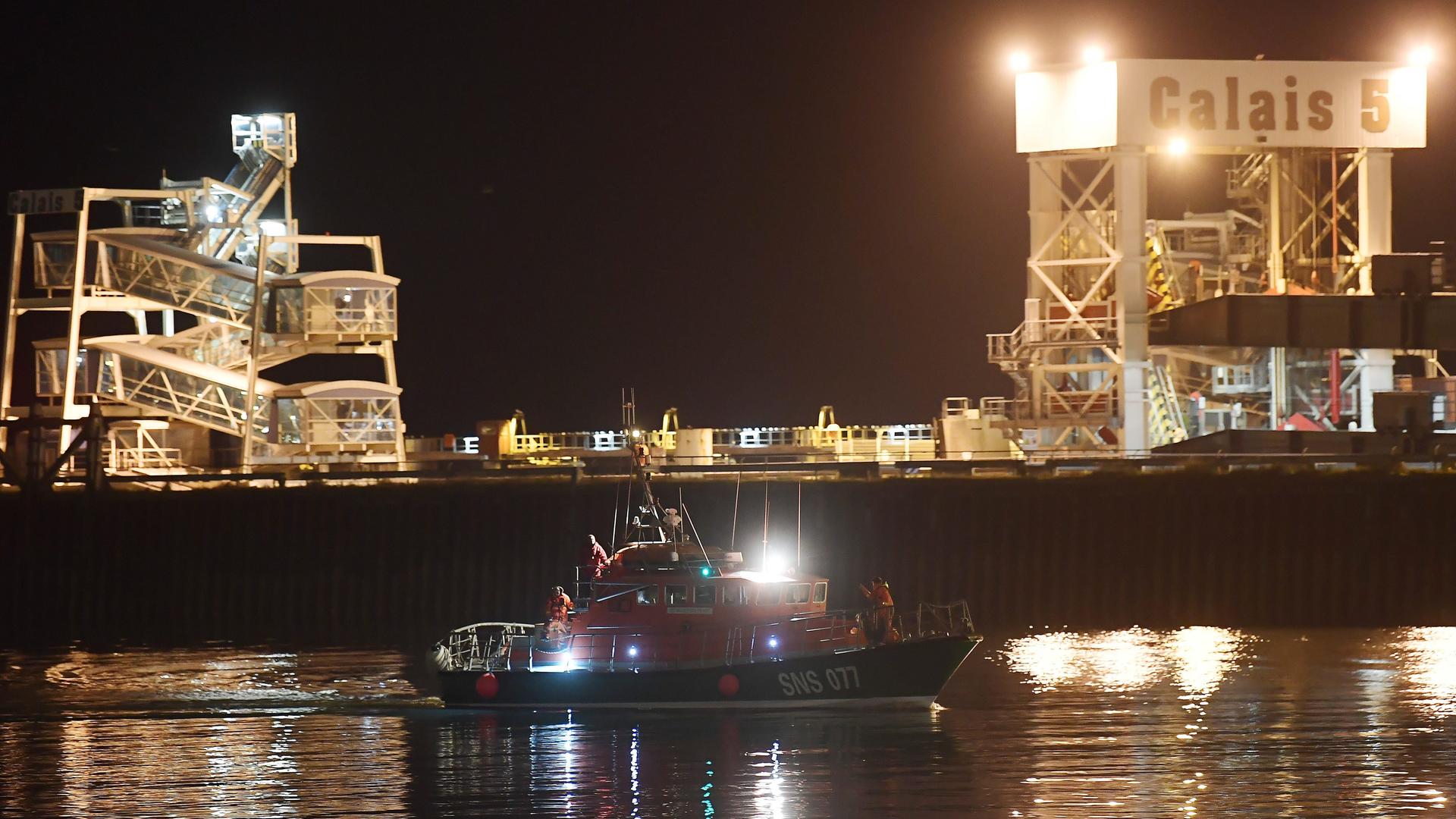 Ein Boot fährt bei Dunkelheit in den Hafen von Calais ein.