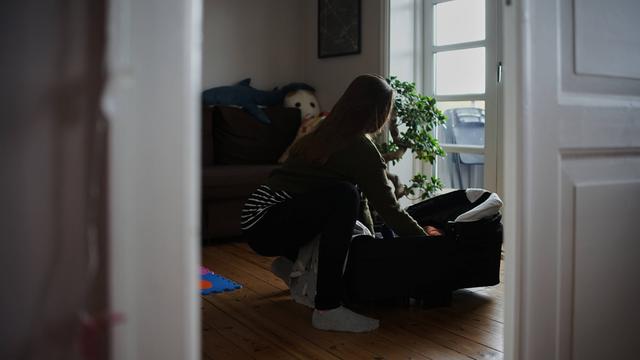 Eine Frau in einer Altbauwohnung beugt sich über eine Babytragetasche.