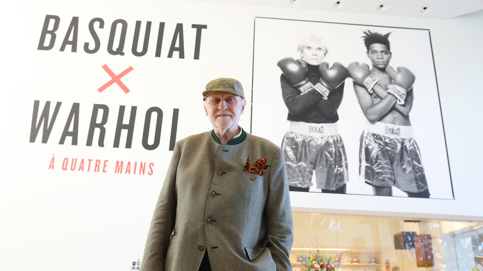 Bruno Bischofberger posiert im Trachtenjanker vor einem Plakat für die Ausstellung "Basquiat X Warhol" in Paris im Jahr 2023 Bruno Bischofberger posiert im Trachtenjanker vor einem Plakat für die Ausstellung "Basquiat X Warhol" in Paris im Jahr 2023