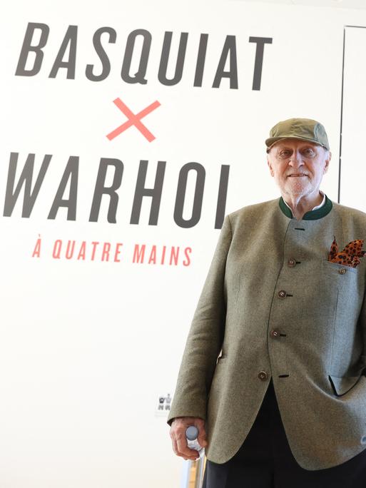 Bruno Bischofberger posiert im Trachtenjanker vor einem Plakat für die Ausstellung "Basquiat X Warhol" in Paris im Jahr 2023