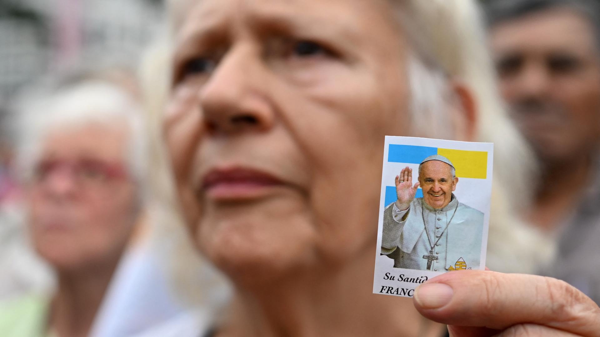 Eine Frau hält ein kleines Foto von Franziskus in ihrer Hand. 