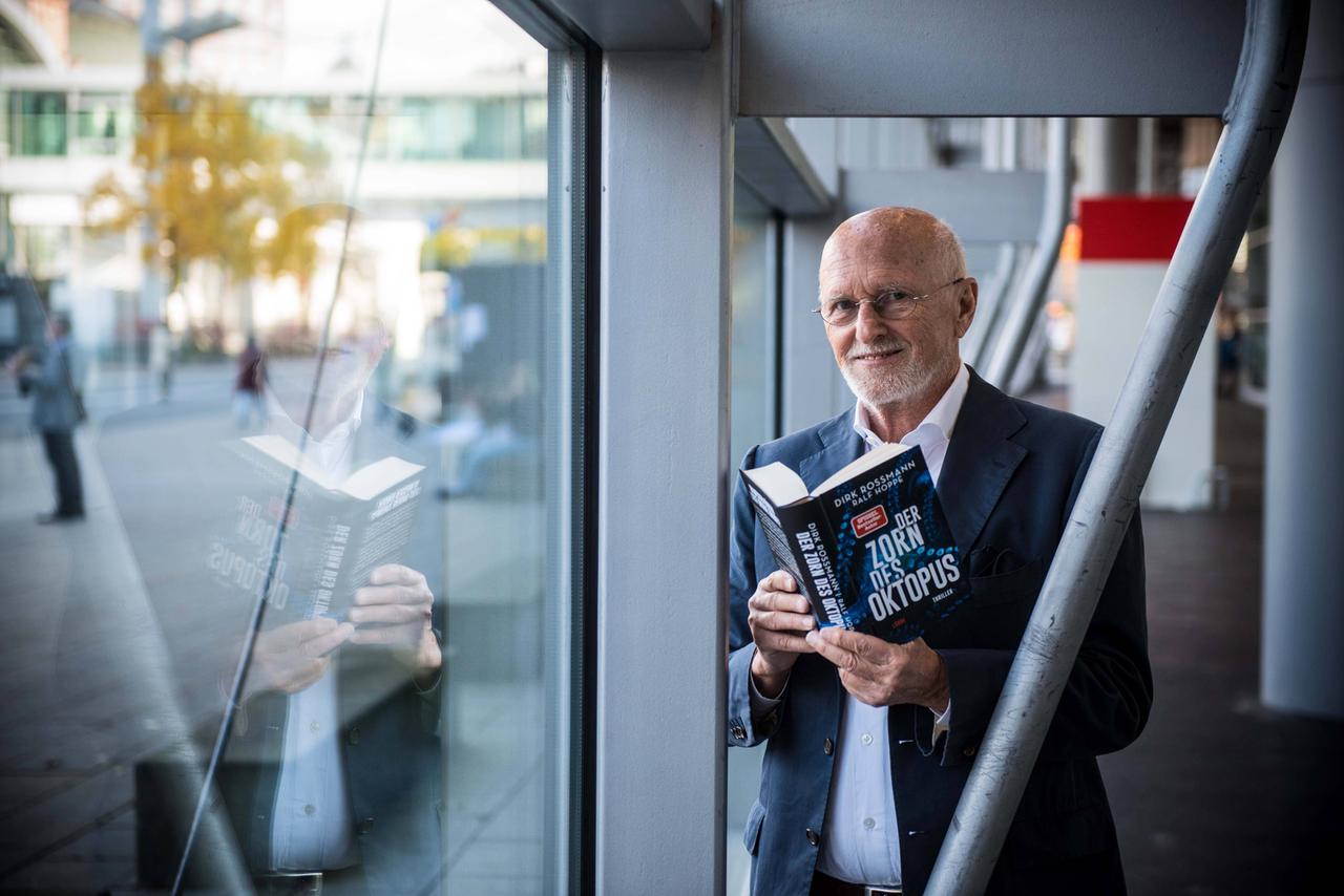Dirk Rossmann steht mit einem aufgeschlagenen Exemplar seines Thrillers "Der Zorn des Oktopus" in einem Gang der Frankfurter Buchmesse.