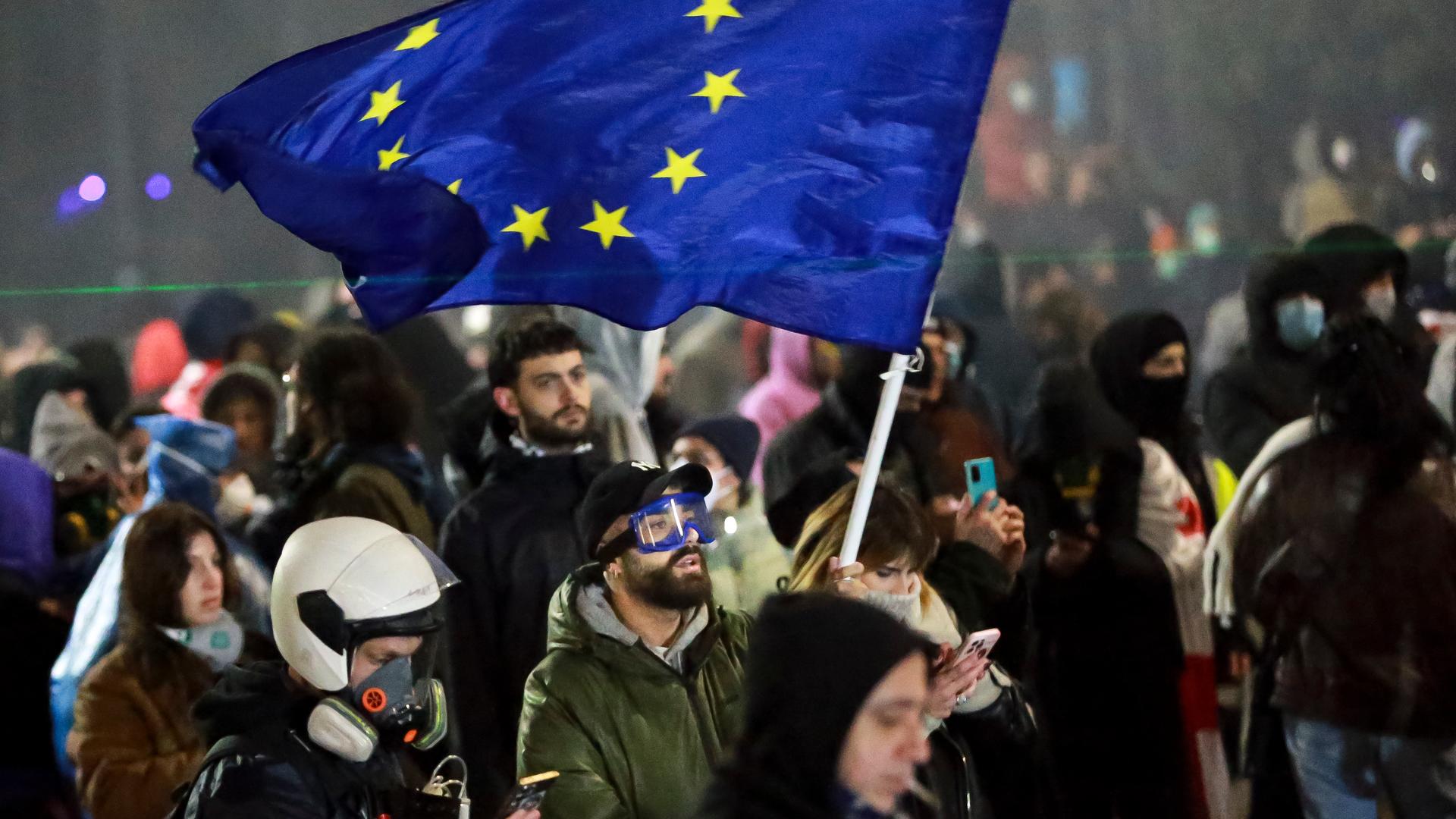 Demonstranten stehen während einer Kundgebung vor dem Parlamentsgebäude. Einer schwenkt eine Europa-Flagge.