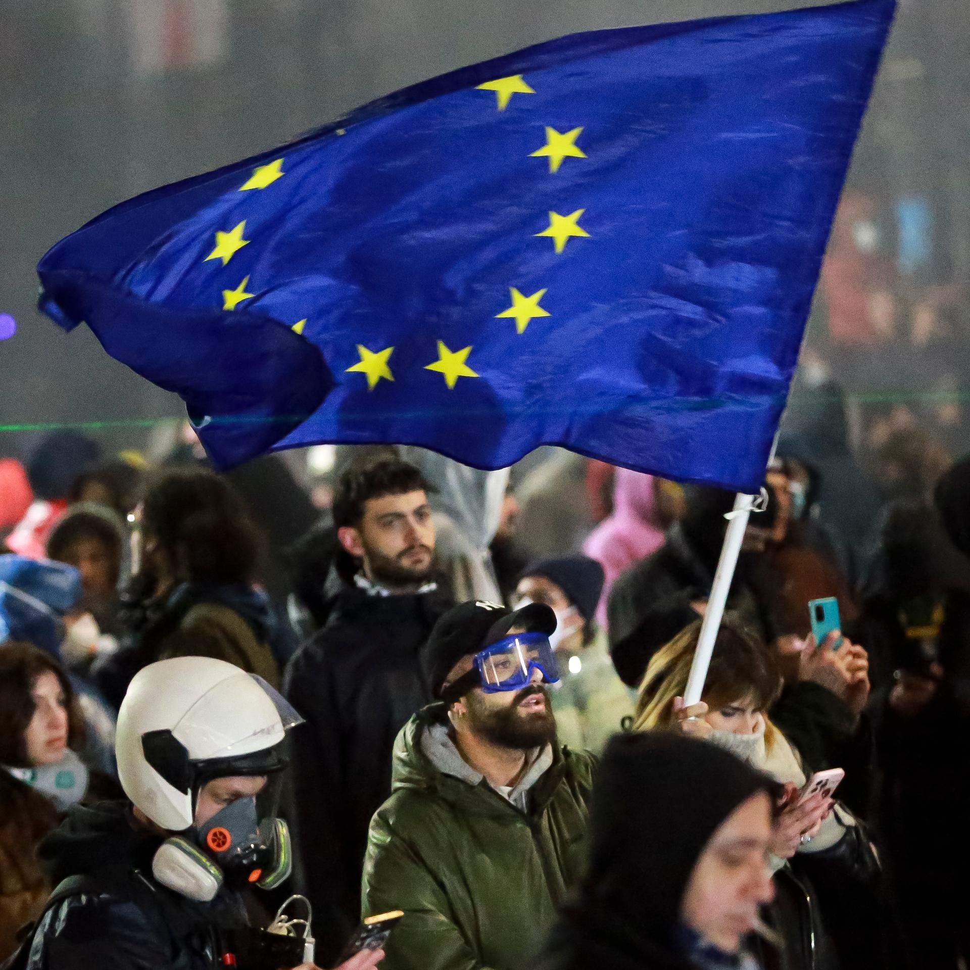 Demonstranten stehen während einer Kundgebung vor dem Parlamentsgebäude. Einer schwenkt eine Europa-Flagge.