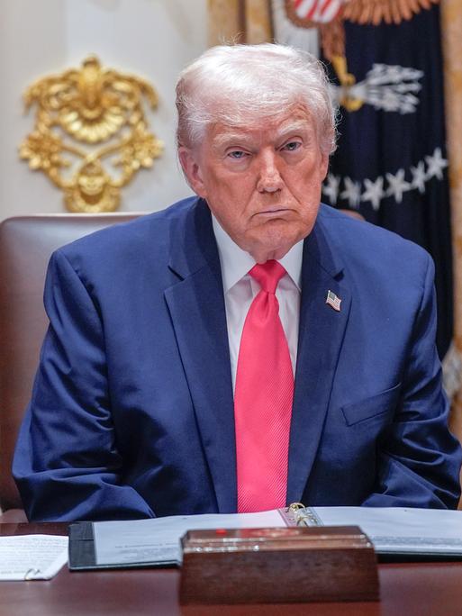 Ein Mann mit weißem Haar sitzt an einem Schreibtisch, dahinter zahlreiche Flaggen: US-Präsident Donald Trump im "Cabinet Room" des Weißen Hauses.
