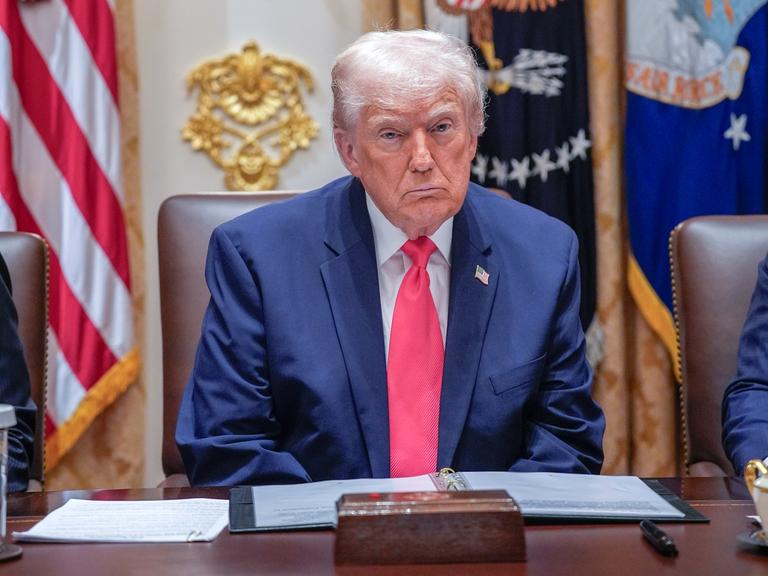 Ein Mann mit weißem Haar sitzt an einem Schreibtisch, dahinter zahlreiche Flaggen: US-Präsident Donald Trump im "Cabinet Room" des Weißen Hauses.