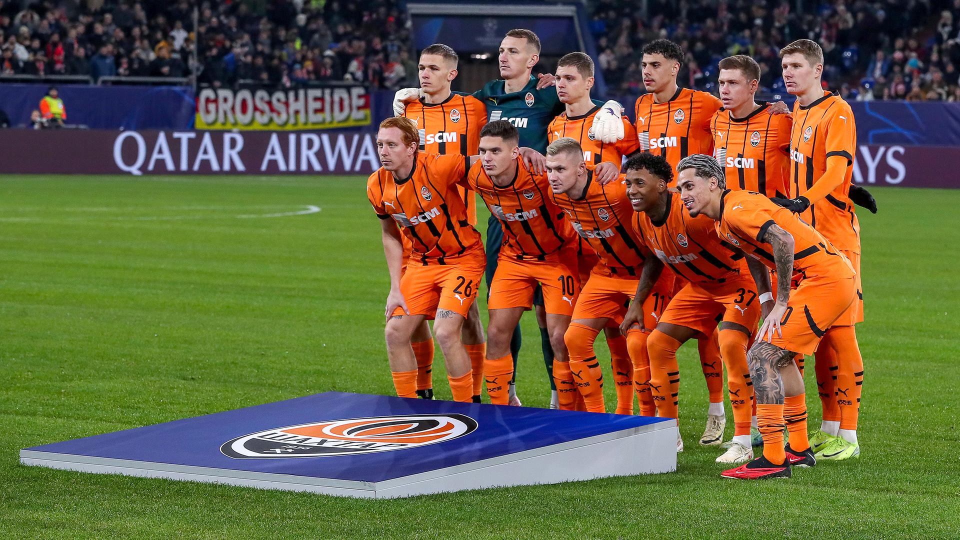 Die Startelf von Shachtar Donezk hat sich in der Arena auf Schalke zum Gruppenfoto aufgestellt. Die Fußballer haben orangefarbene Trikots an.