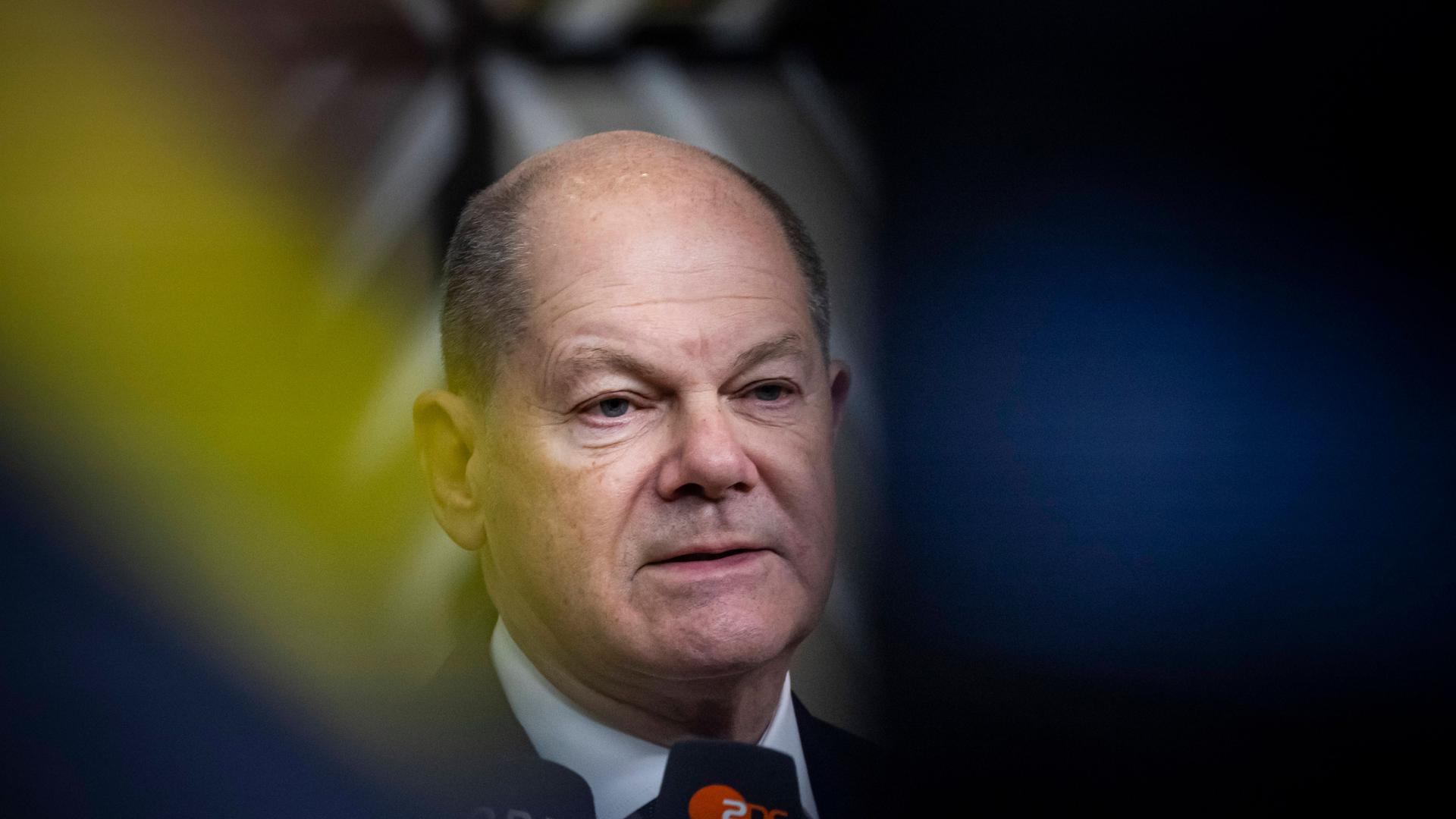 Porträtaufnahme von Bundeskanzler Olaf Scholz, umgeben von sanften gelb und blauen Farben wie in der Ukraine-Flagge.