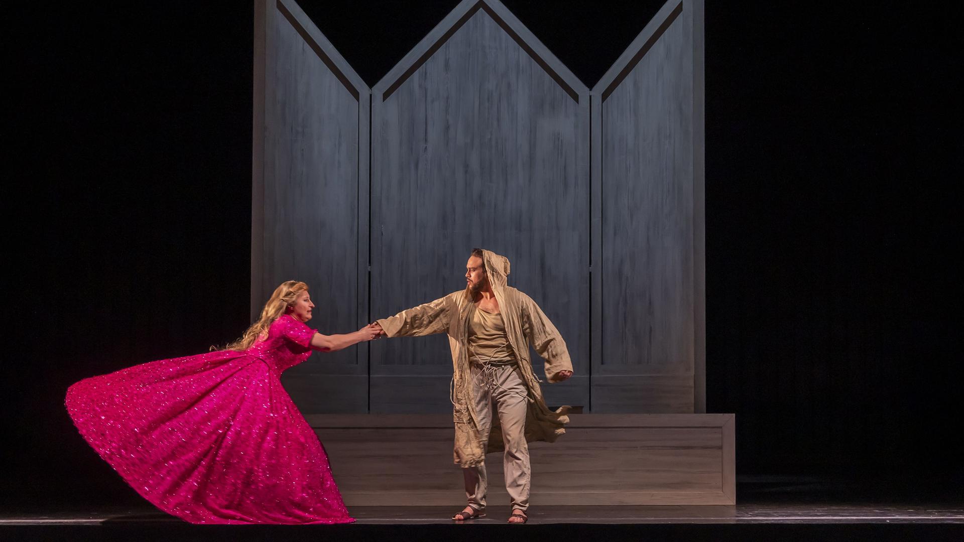 Foto von der Aufführung "Le petit pauvre d'Assise". Eine Frau im pinken Kleid hält sich darin an einem in Lumpen gekleideten Mann fest. 