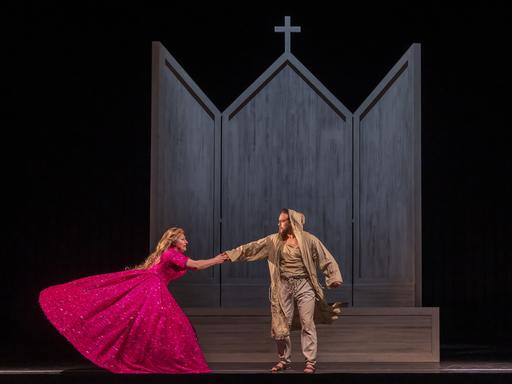 Foto von der Aufführung "Le petit pauvre d'Assise". Eine Frau im pinken Kleid hält sich darin an einem in Lumpen gekleideten Mann fest. 