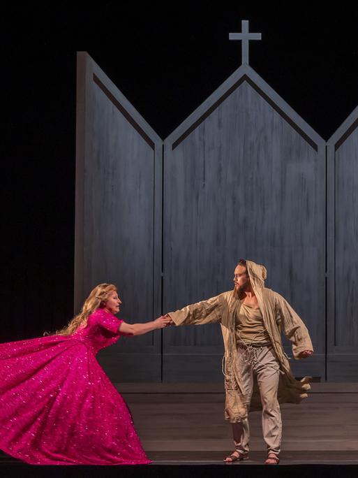 Foto von der Aufführung "Le petit pauvre d'Assise". Eine Frau im pinken Kleid hält sich darin an einem in Lumpen gekleideten Mann fest. 