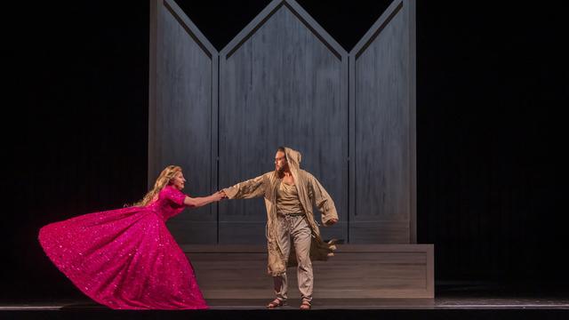 Foto von der Aufführung "Le petit pauvre d'Assise". Eine Frau im pinken Kleid hält sich darin an einem in Lumpen gekleideten Mann fest. 