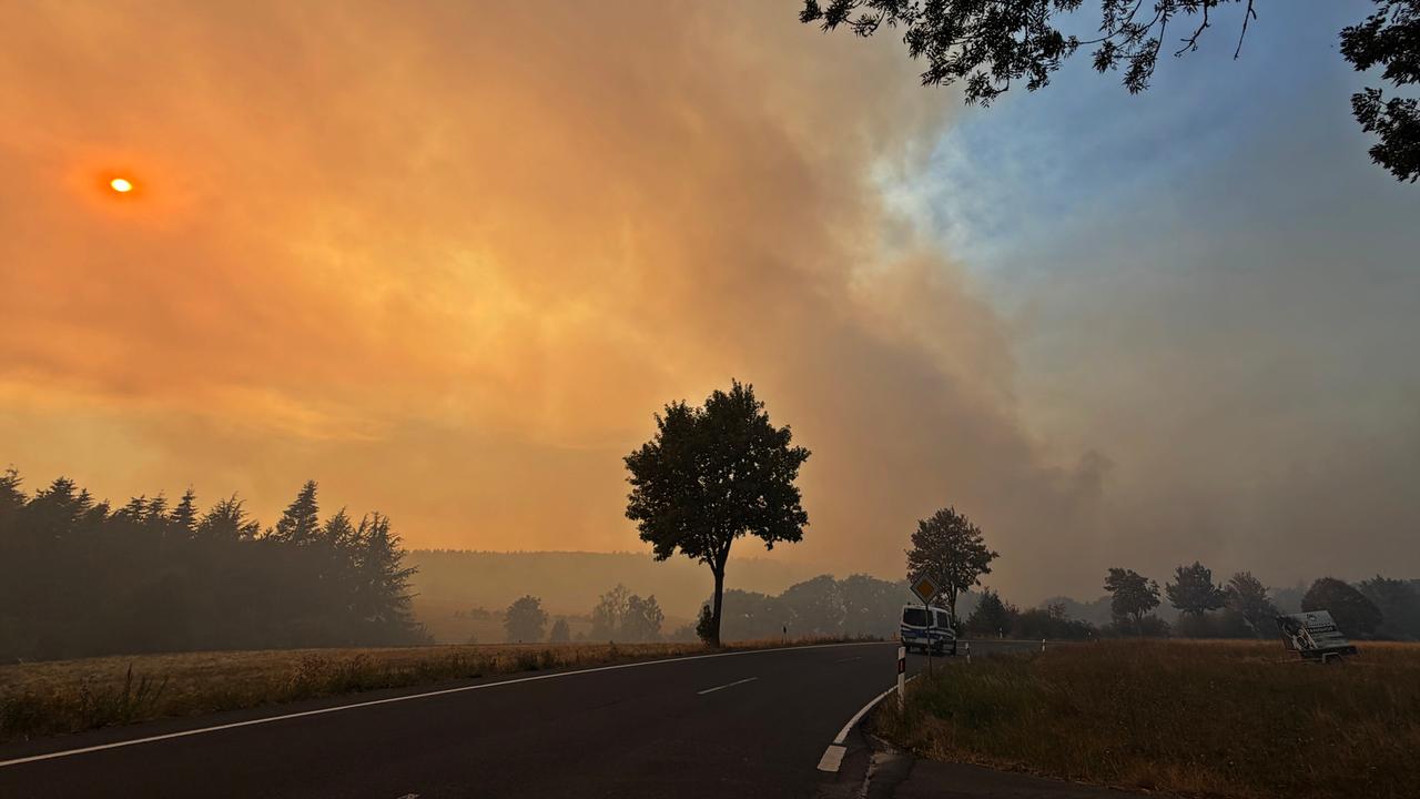 Rauchschwaden und Feuerschein über einer Landstraße, auf der ein Polizeiauto fährt: Waldbrand im Hürtgenwald Rauchschwaden und Feuerschein über einer Landstraße, auf der ein Polizeiauto fährt: Waldbrand im Hürtgenwald