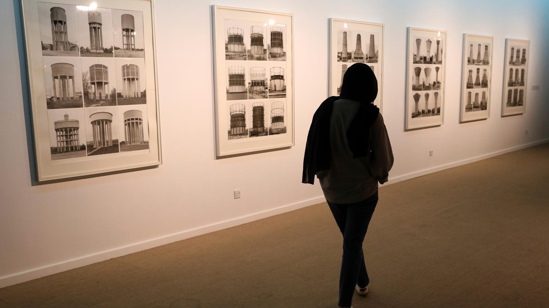 Die Besucherin einer Ausstellung steht vor Bildern der Fotografen Bernd und Hilla Becher