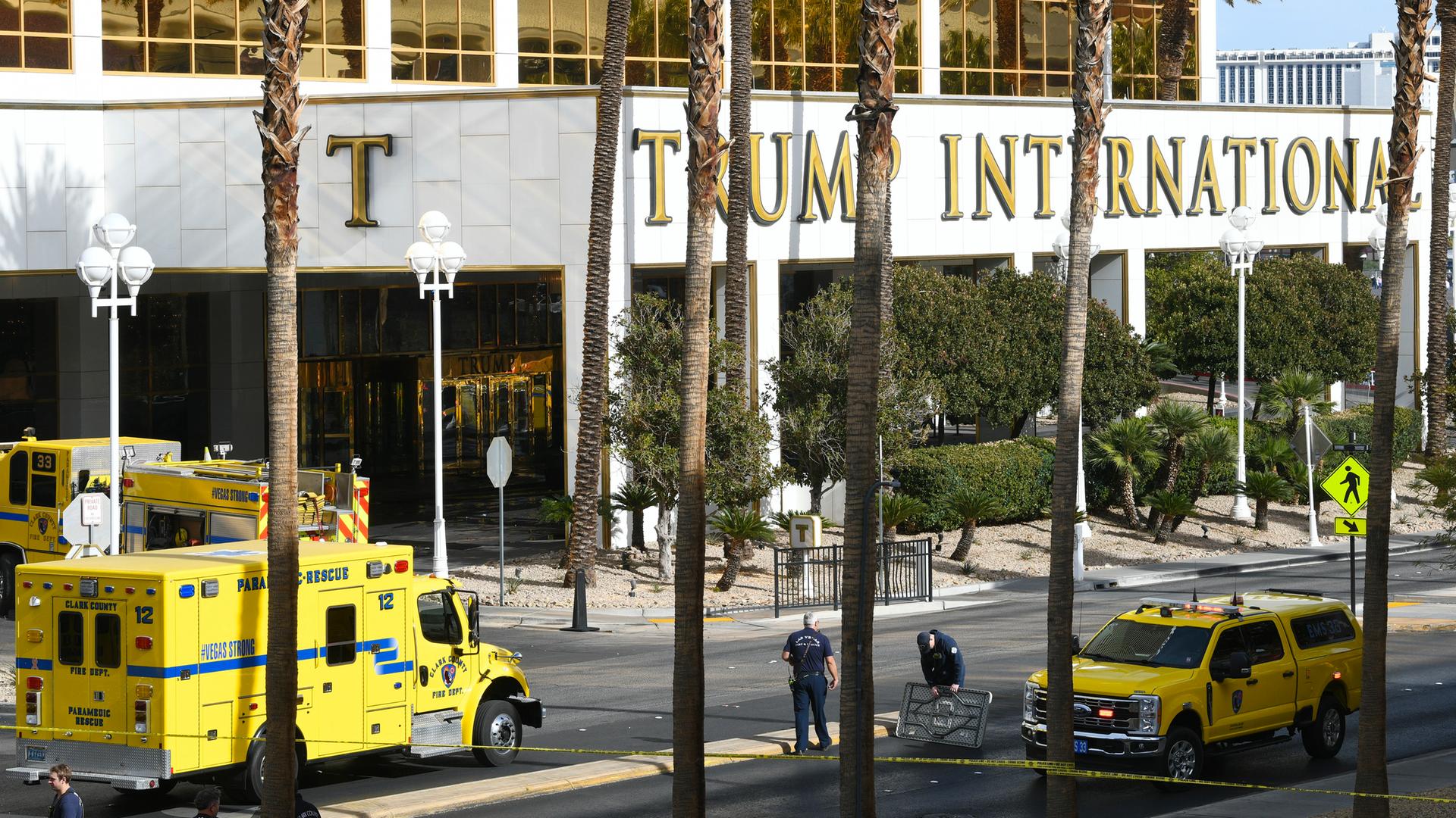 Blick aus einiger Entfernung auf zwei gelbe Feuerwehrfahrzeuge vor dem Eingang des Hotels mit der Aufschrift "Trump International". Im Vordergrund Palmen.